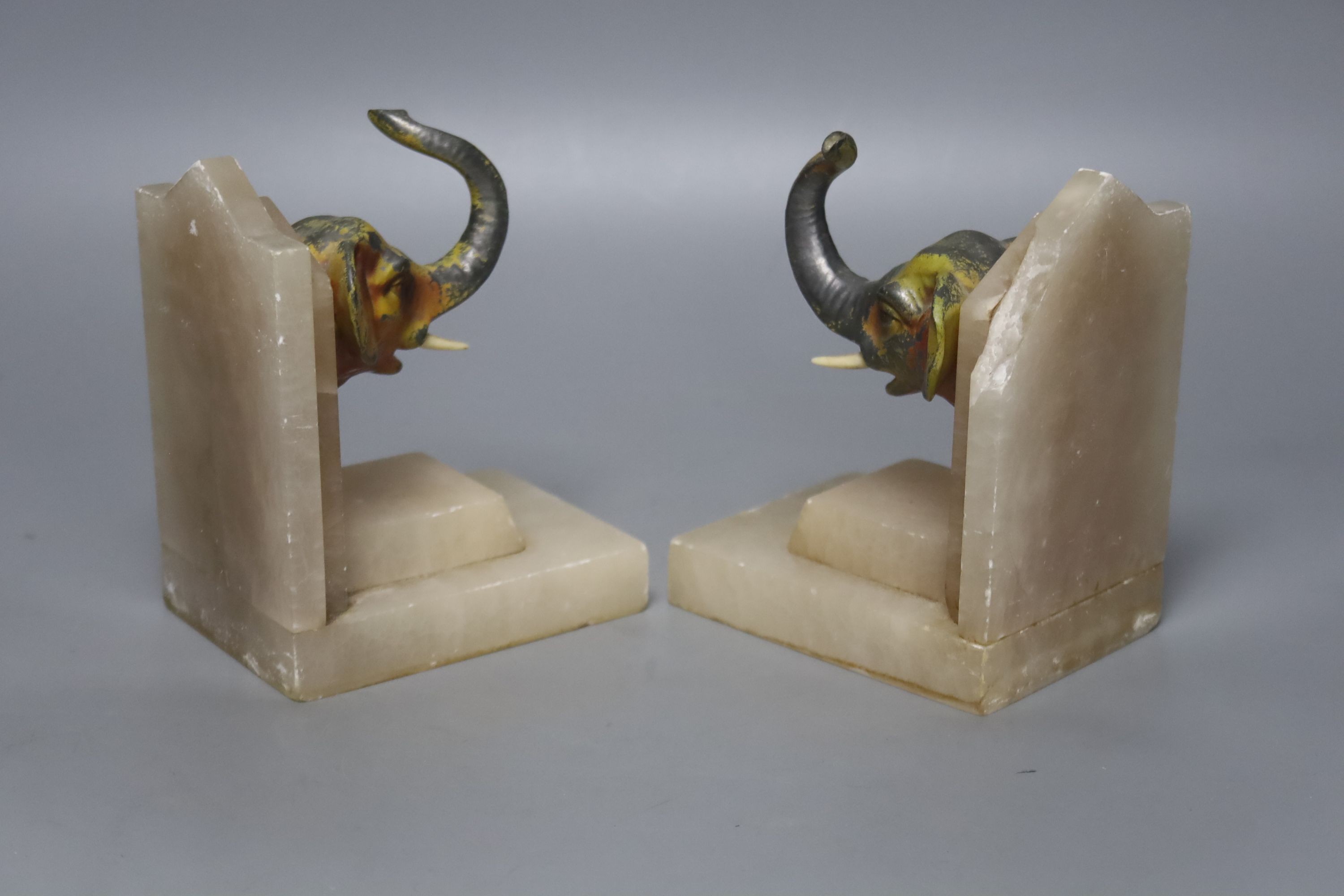 A pair of 1930's alabaster book ends, each applied with a painted metal elephant head, 14cm